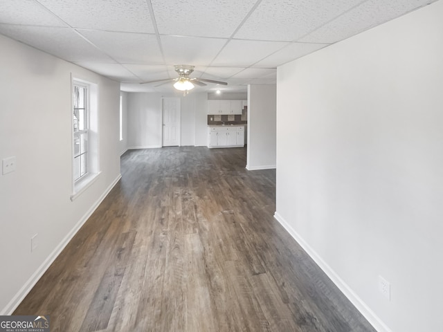 unfurnished living room featuring a drop ceiling, dark wood-type flooring, and ceiling fan