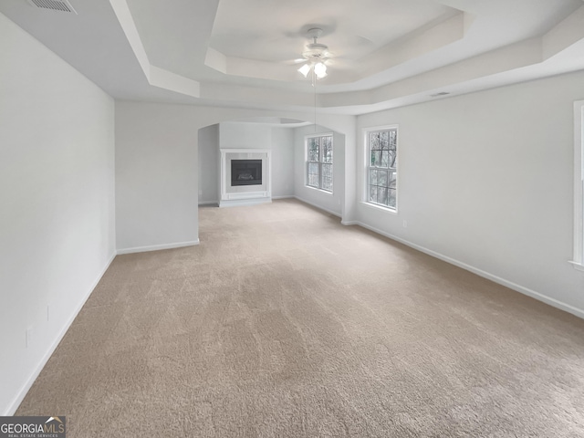 unfurnished living room with light colored carpet, ceiling fan, and a tray ceiling