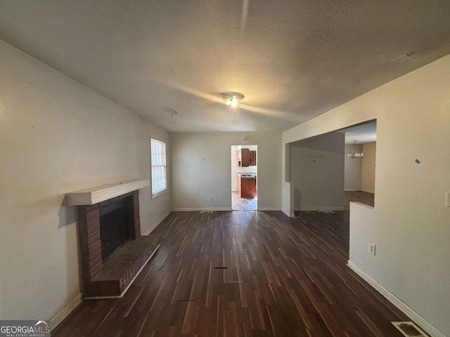 unfurnished living room featuring a brick fireplace, a textured ceiling, and dark hardwood / wood-style flooring