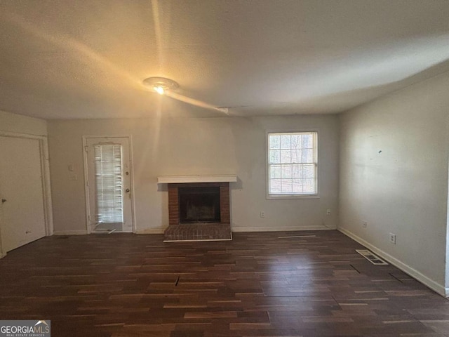 unfurnished living room featuring a brick fireplace, dark wood-type flooring, and a textured ceiling