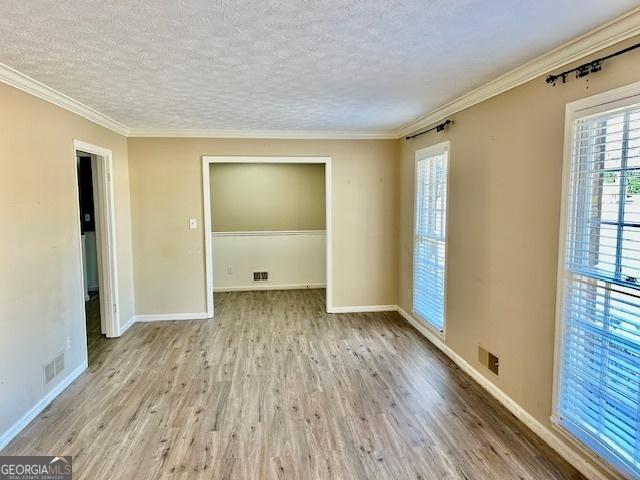 empty room featuring crown molding, a textured ceiling, and light hardwood / wood-style flooring