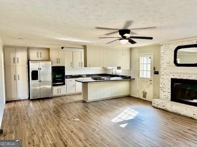 kitchen with light wood-type flooring, stainless steel fridge, kitchen peninsula, a fireplace, and oven