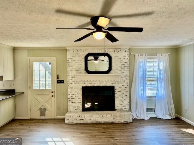 unfurnished living room with ornamental molding, a brick fireplace, wood-type flooring, and a wealth of natural light