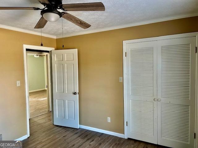 unfurnished bedroom featuring ceiling fan, dark hardwood / wood-style floors, ornamental molding, a textured ceiling, and a closet