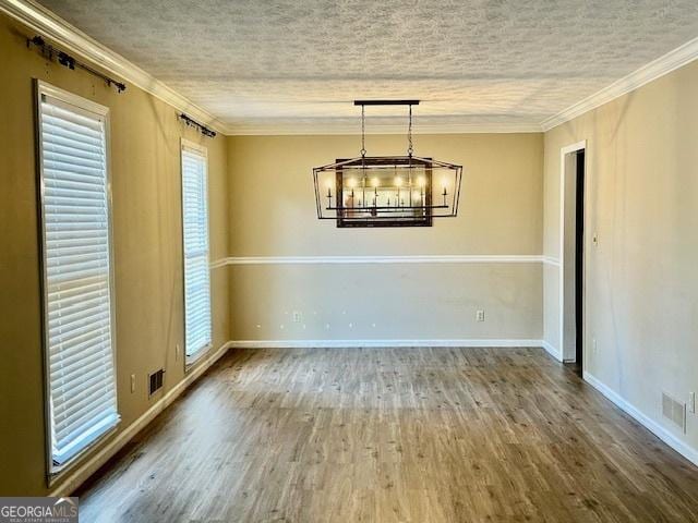 unfurnished dining area with hardwood / wood-style flooring, ornamental molding, a notable chandelier, and a textured ceiling