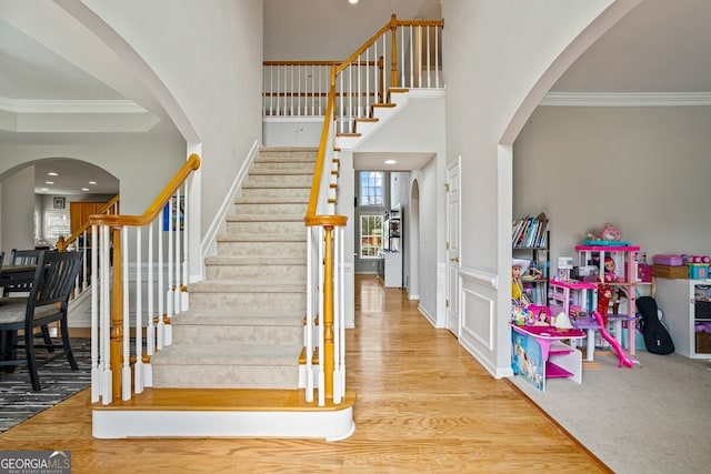 staircase with ornamental molding, wood-type flooring, and a high ceiling