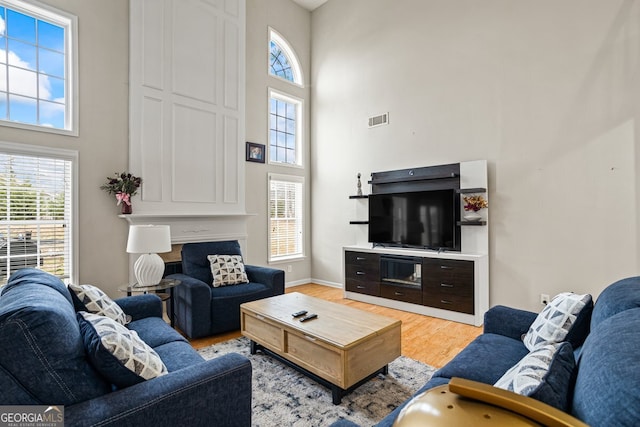 living room with a towering ceiling, a healthy amount of sunlight, and light hardwood / wood-style flooring