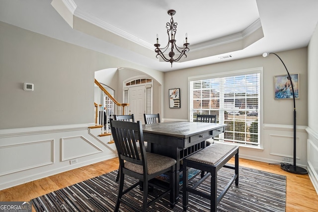 dining area featuring a raised ceiling, ornamental molding, hardwood / wood-style floors, and a chandelier