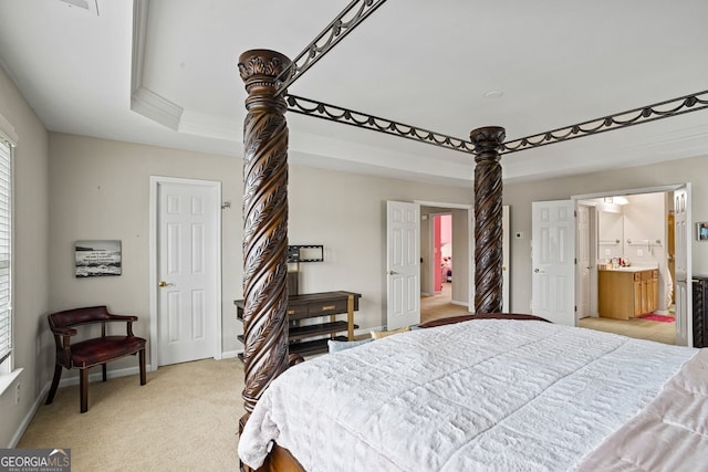 bedroom with a raised ceiling, light colored carpet, and ensuite bath