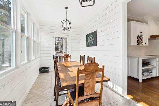 dining space featuring a notable chandelier, crown molding, and wooden walls