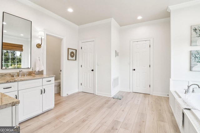 bathroom featuring tiled tub, crown molding, vanity, wood-type flooring, and toilet