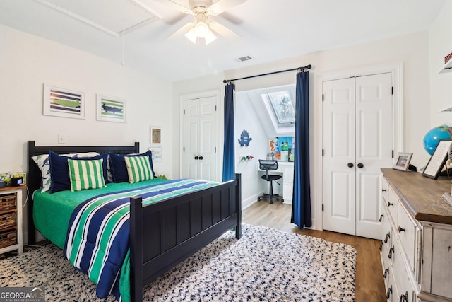 bedroom with ceiling fan, light hardwood / wood-style floors, and two closets