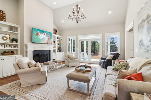 living room featuring wood-type flooring, a chandelier, high vaulted ceiling, and built in shelves