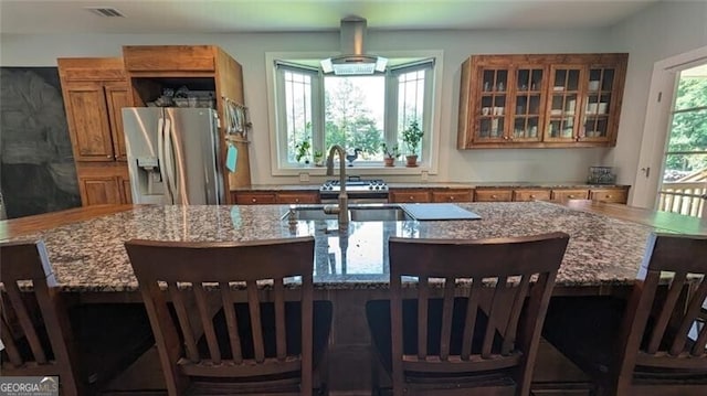 kitchen featuring sink, a breakfast bar area, a large island with sink, light stone counters, and stainless steel refrigerator with ice dispenser