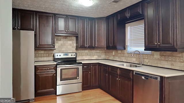 kitchen with sink, backsplash, light hardwood / wood-style floors, and appliances with stainless steel finishes