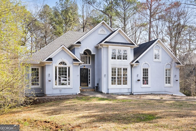 view of front of home with roof with shingles, a front lawn, and stucco siding