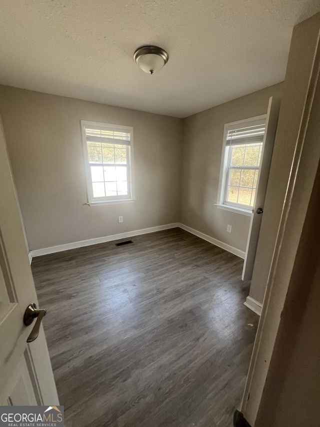 unfurnished room featuring dark wood-type flooring and a textured ceiling