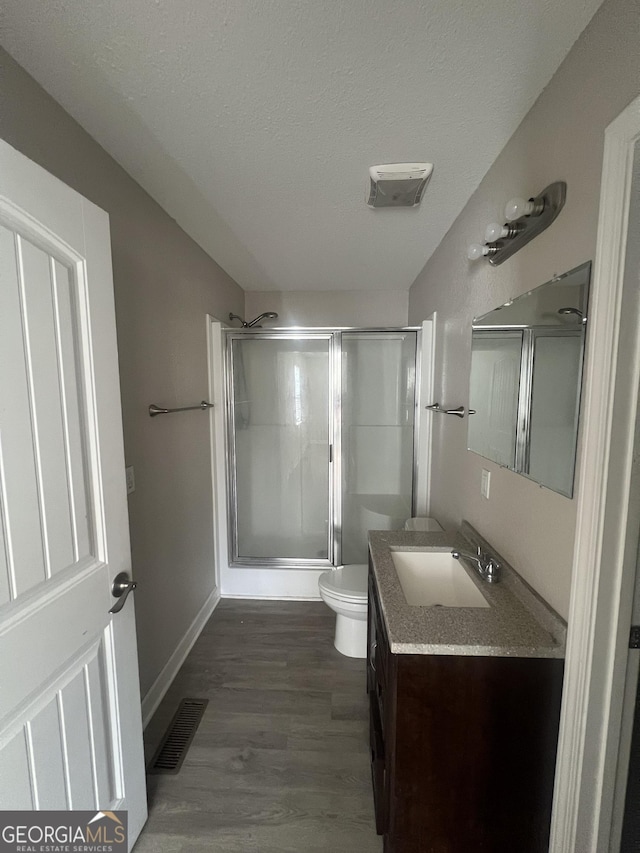 bathroom with wood-type flooring, vanity, walk in shower, toilet, and a textured ceiling