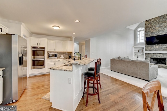 kitchen with a kitchen bar, sink, white cabinetry, appliances with stainless steel finishes, and a fireplace