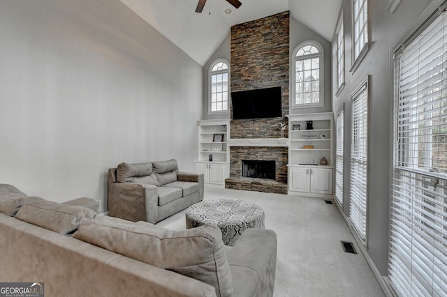 carpeted living room with ceiling fan, a stone fireplace, and high vaulted ceiling