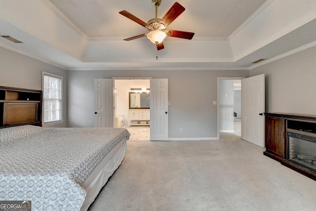 carpeted bedroom featuring ceiling fan, ensuite bath, ornamental molding, and a tray ceiling