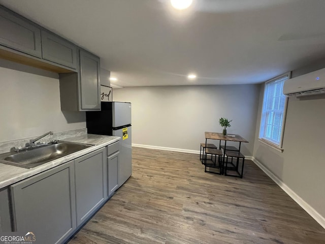 kitchen with dark wood-type flooring, sink, gray cabinetry, a wall mounted air conditioner, and refrigerator