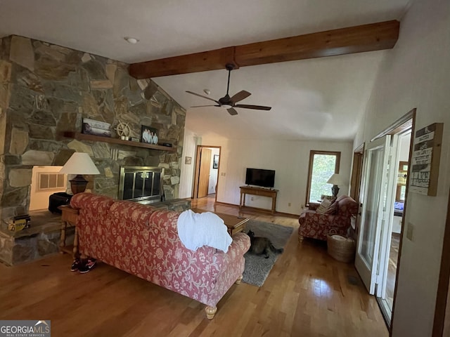 living room featuring beamed ceiling, a stone fireplace, ceiling fan, and light hardwood / wood-style flooring