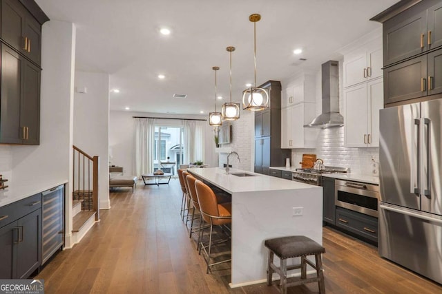 kitchen with wine cooler, wall chimney exhaust hood, white cabinetry, high end refrigerator, and a center island with sink