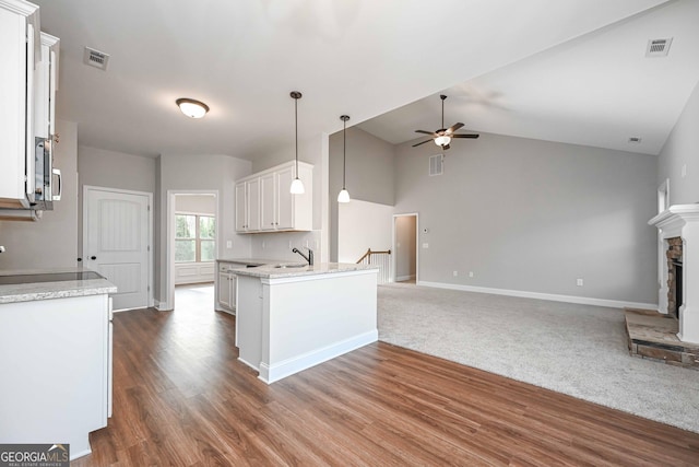 kitchen featuring white cabinetry, decorative light fixtures, a stone fireplace, ceiling fan, and light stone counters