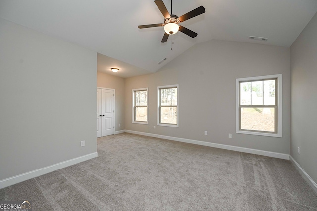 carpeted spare room featuring a healthy amount of sunlight, vaulted ceiling, and ceiling fan