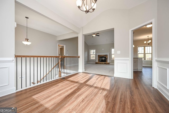 spare room with a fireplace, lofted ceiling, hardwood / wood-style floors, and ceiling fan with notable chandelier