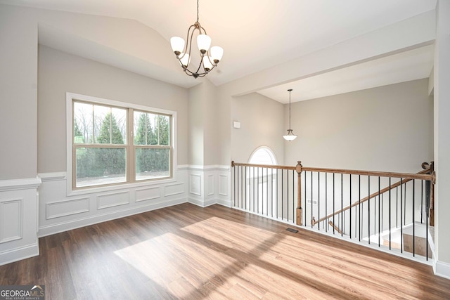 spare room with a notable chandelier, plenty of natural light, vaulted ceiling, and hardwood / wood-style floors