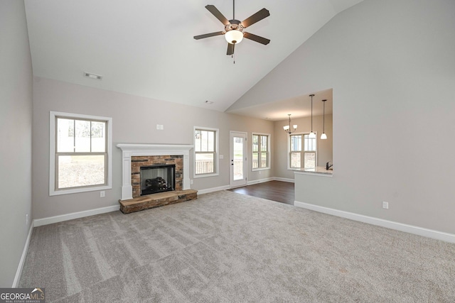 unfurnished living room with a fireplace, high vaulted ceiling, carpet, and ceiling fan with notable chandelier