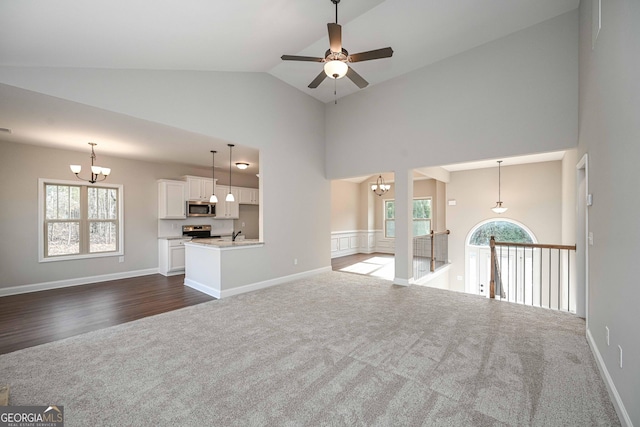 unfurnished living room with high vaulted ceiling, dark colored carpet, and a wealth of natural light