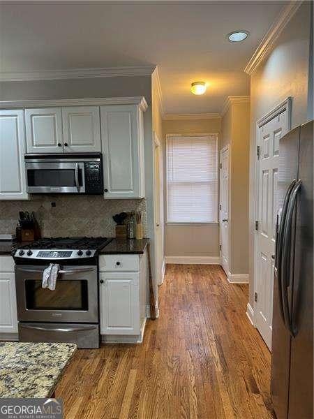 kitchen featuring white cabinetry, stainless steel appliances, crown molding, and hardwood / wood-style floors