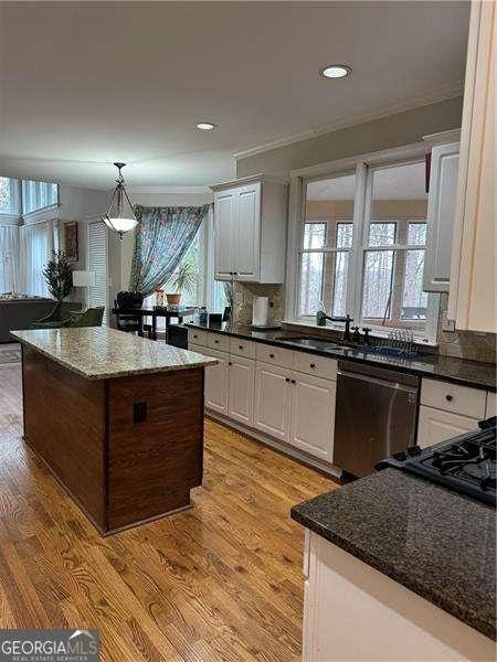 kitchen with sink, dishwasher, white cabinets, dark stone counters, and light wood-type flooring