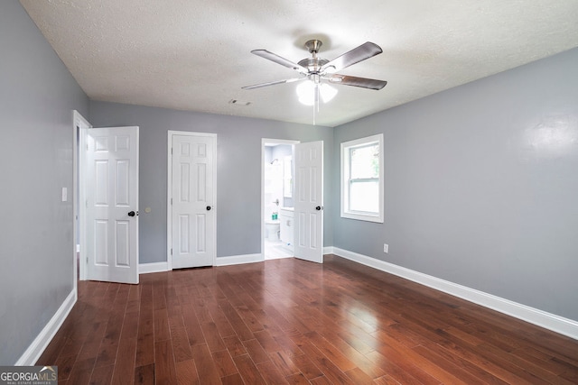 unfurnished bedroom featuring dark wood-type flooring, ensuite bath, ceiling fan, and a textured ceiling