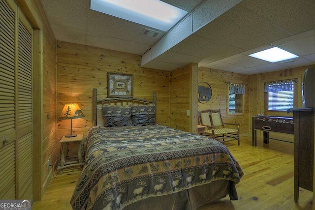 bedroom with a paneled ceiling, light wood-type flooring, and wood walls