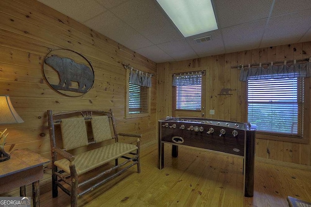 living area with hardwood / wood-style flooring, wooden walls, a drop ceiling, and a wealth of natural light