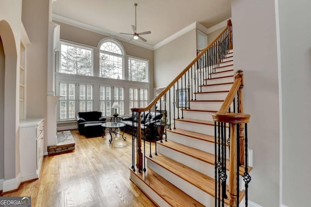 stairs with crown molding, plenty of natural light, a towering ceiling, and hardwood / wood-style flooring