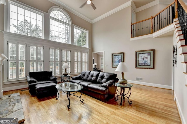 living room featuring crown molding, wood-type flooring, a healthy amount of sunlight, and a towering ceiling