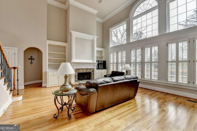 living room with a towering ceiling, a fireplace, ornamental molding, and light wood-type flooring