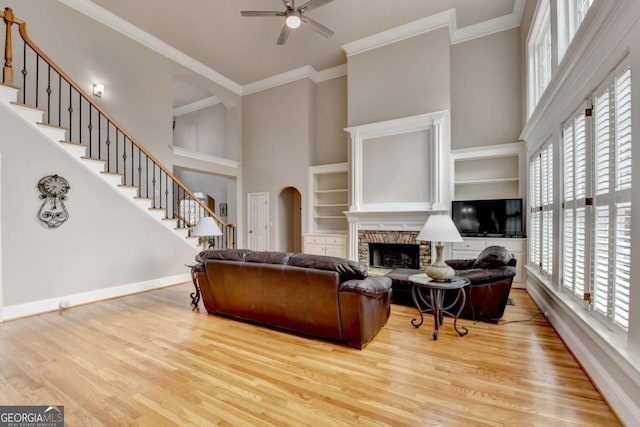 living room featuring a towering ceiling, ornamental molding, a stone fireplace, and light hardwood / wood-style floors