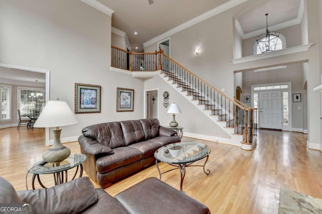 living room with ornamental molding, light hardwood / wood-style floors, a high ceiling, and a notable chandelier