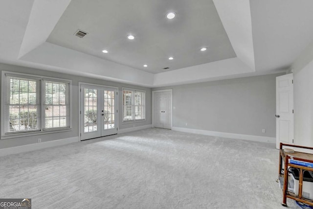 unfurnished living room featuring a raised ceiling, light colored carpet, and french doors