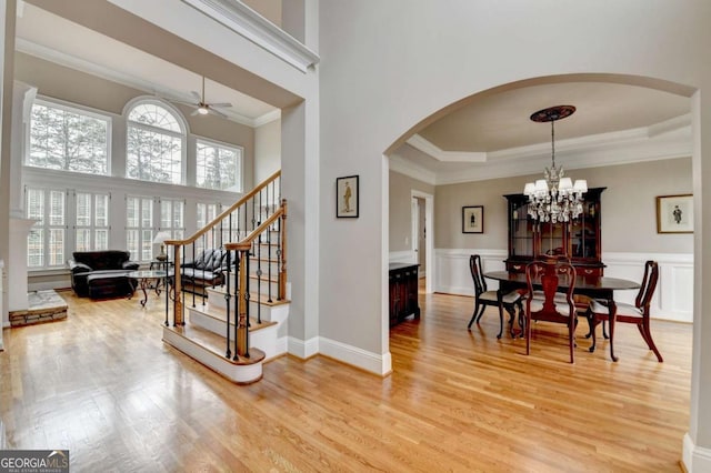 interior space with ornamental molding, wood-type flooring, ceiling fan with notable chandelier, and a high ceiling