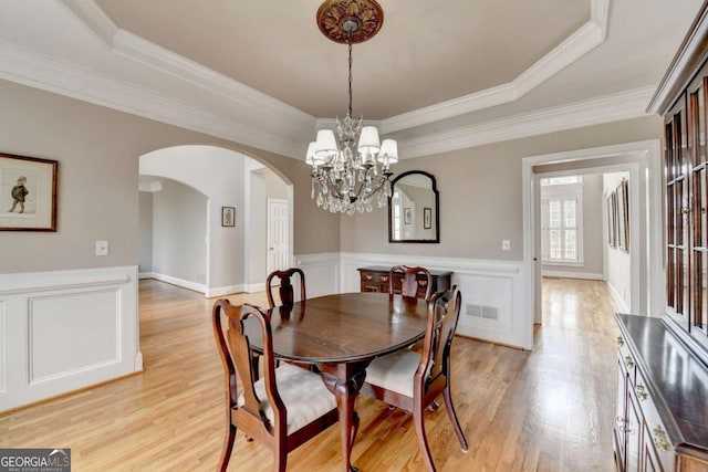 dining space with ornamental molding, a raised ceiling, and light wood-type flooring