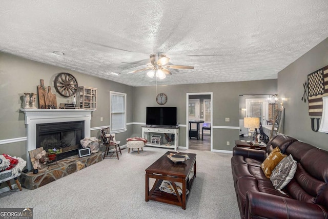 living room featuring ceiling fan, carpet flooring, a fireplace, and a textured ceiling