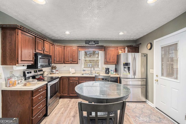 kitchen featuring sink, light hardwood / wood-style flooring, a textured ceiling, and appliances with stainless steel finishes