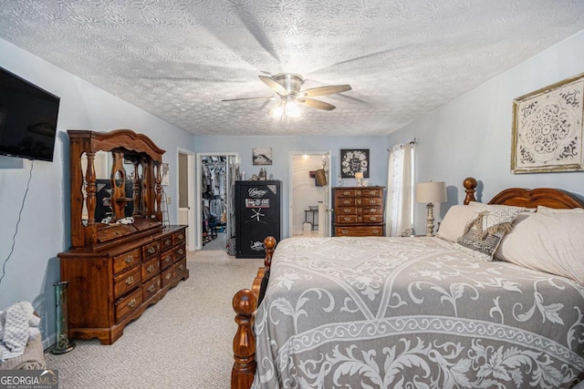 bedroom with ceiling fan, a textured ceiling, light carpet, a walk in closet, and a closet